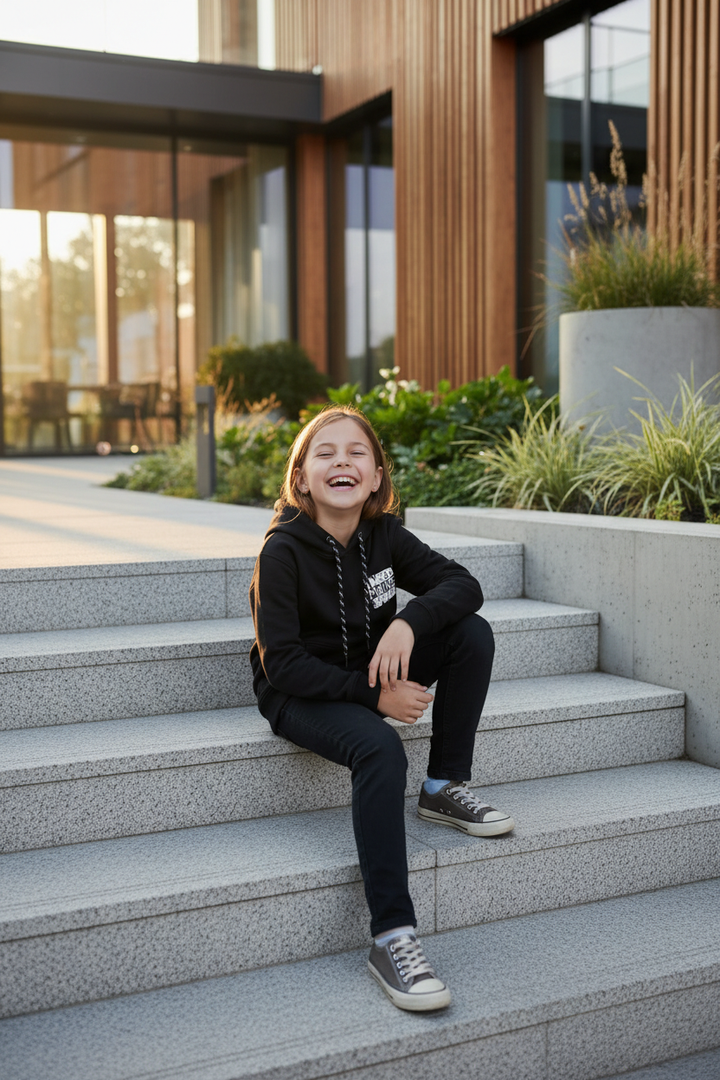 Enfant portant le hoodie noir CHAYA STYLE, assise sur des marches, extérieur chic