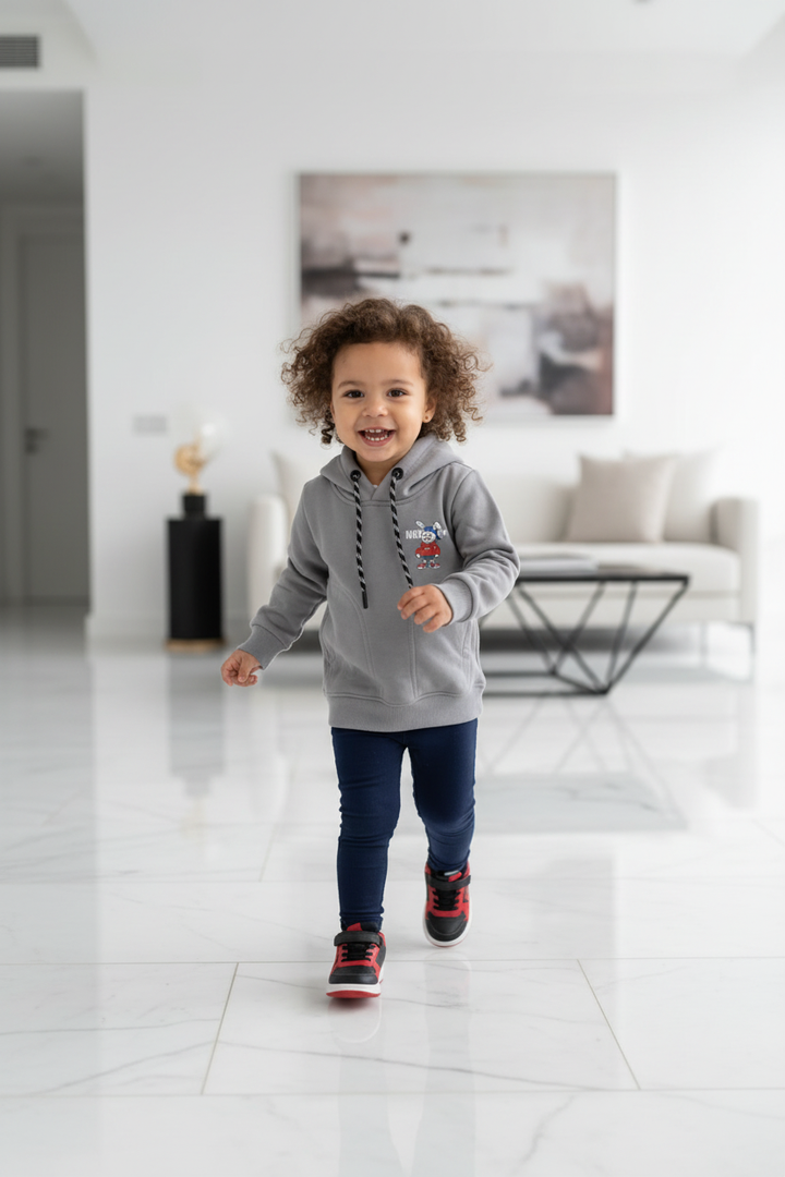 Petite fille métisse portant le hoodie gris unisexe CHAYA STYLE, pose en mouvement, intérieur moderne